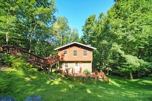 Une cabane en bois à deux étages, dotée d’une terrasse et d’un escalier, entour ée d’une forêt dense.