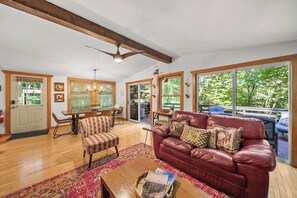 A spacious living room with a leather sofa, a dining area, and a large window offering a view of the outdoors. - The Barking Beech: Pet Friendly, Hot Tub, Firepit, Fenced Yard, 4 TVs! (Banner Elk)
