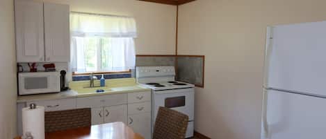 Cozinha compacta com armários brancos, micro-ondas, fogão e geladeira.
