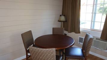 A round wooden table with four chairs, a lamp, and a window with curtains.