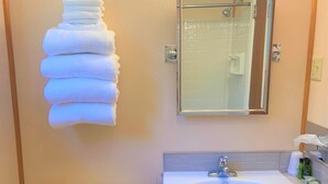 A bathroom with a toilet, a sink, a mirror, and a stack of towels.