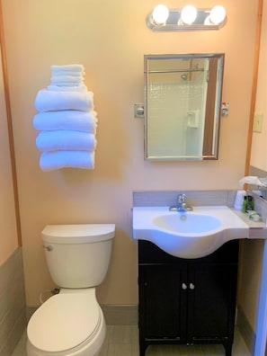 Un baño con inodoro, lavabo, espejo y una pila de toallas.