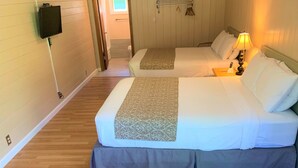 A hotel room with two beds, a TV mounted on the wall, a bedside table with a lamp, and a wooden floor.