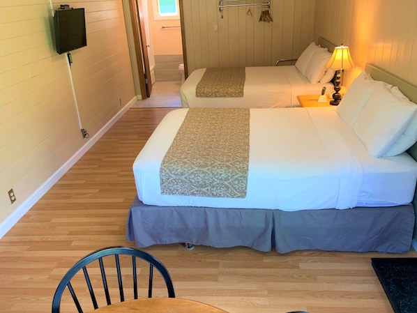 Una habitación de hotel con dos camas, un televisor montado en la pared, una mesita de noche con lámpara y suelo de madera.
