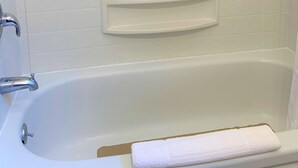 A white bathtub with a chrome faucet, a white towel, and a small shelf above it.