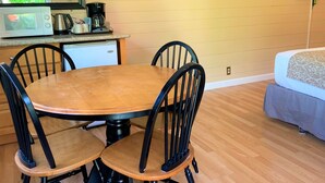 A dining area with a wooden table and chairs, a microwave, a coffee maker, and a small refrigerator.