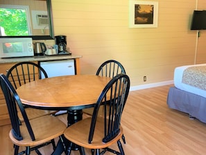 Un comedor con mesa y sillas de madera, microondas, cafetera y refrigerador pequeño.