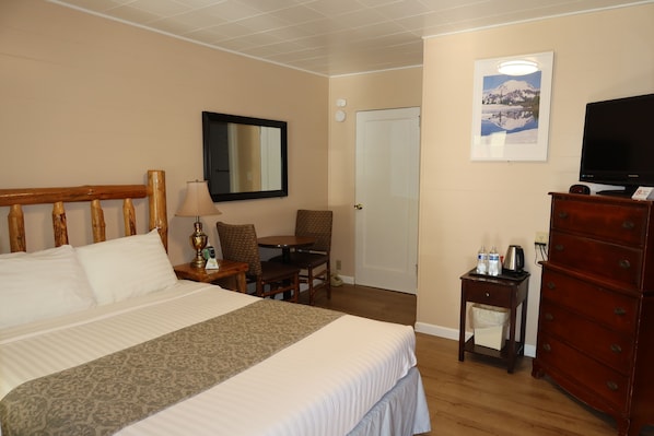 Habitación de hotel con cama, escritorio, silla, cómoda, televisor y un cuadro en la pared.