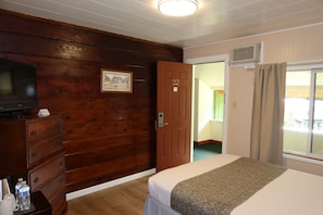 Habitación de hotel con paneles de madera, una cama con una colcha estampada, un aparador con televisor y una puerta con el número 22.