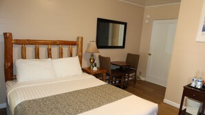 Una habitación de hotel con una cama, una mesita de noche, una silla, una mesa y una puerta.
