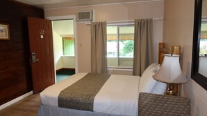 Una habitación de hotel con una cama, una silla, una lámpara, una puerta y un ventanal con cortinas.