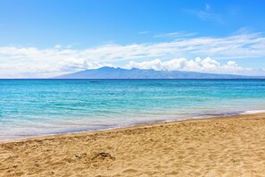 A beach with clear turquoise water, a sandy shore, and distant mountains under a blue sky. - Chic, Upgraded 2BR with Stunning Ocean Views (Lahaina)