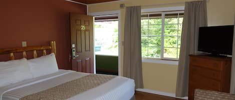 Habitación de hotel con cama, televisión, cómoda de madera y ventana con cortinas.