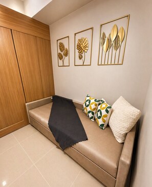 Ein Zimmer mit einem beigen Sofa, einer schwarzen Decke und gemusterten Kissen.