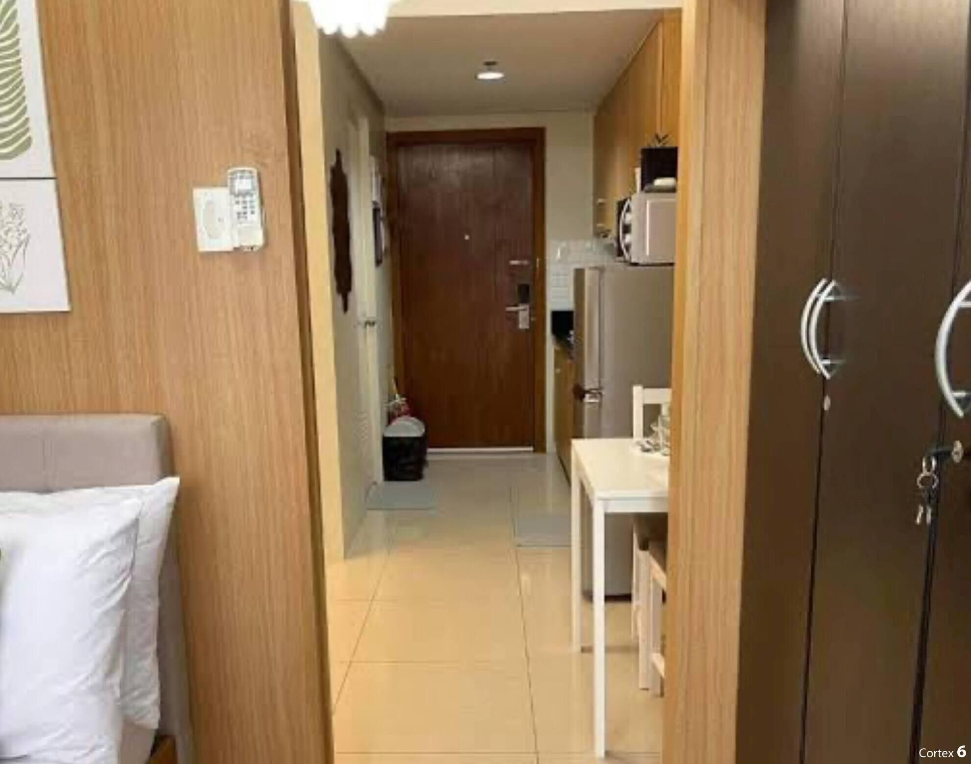 Un pasillo estrecho con una puerta de madera, un teléfono blanco instalado en la pared y una pequeña mesa con cubierta blanca.