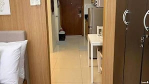 Un pasillo estrecho con una puerta de madera, un teléfono blanco instalado en la pared y una pequeña mesa con cubierta blanca.