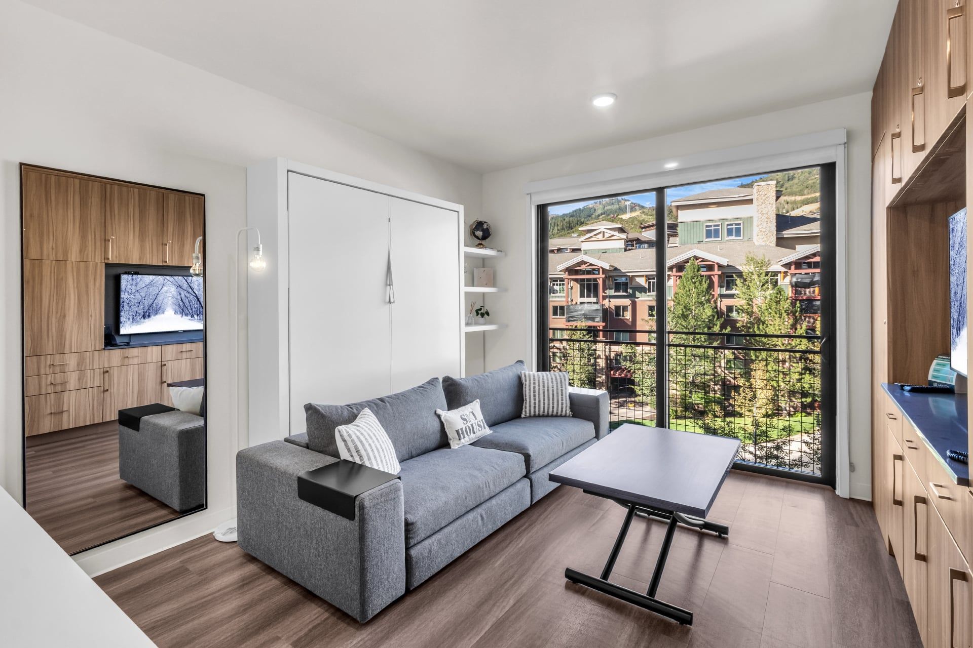 A modern living room with a grey sectional sofa, a small table, and a TV mounted on a wooden cabinet.