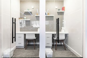 Une salle de bain moderne avec un meuble-lavabo blanc, deux chaises blanches, un miroir et une étagère contenant des articles de toilette.