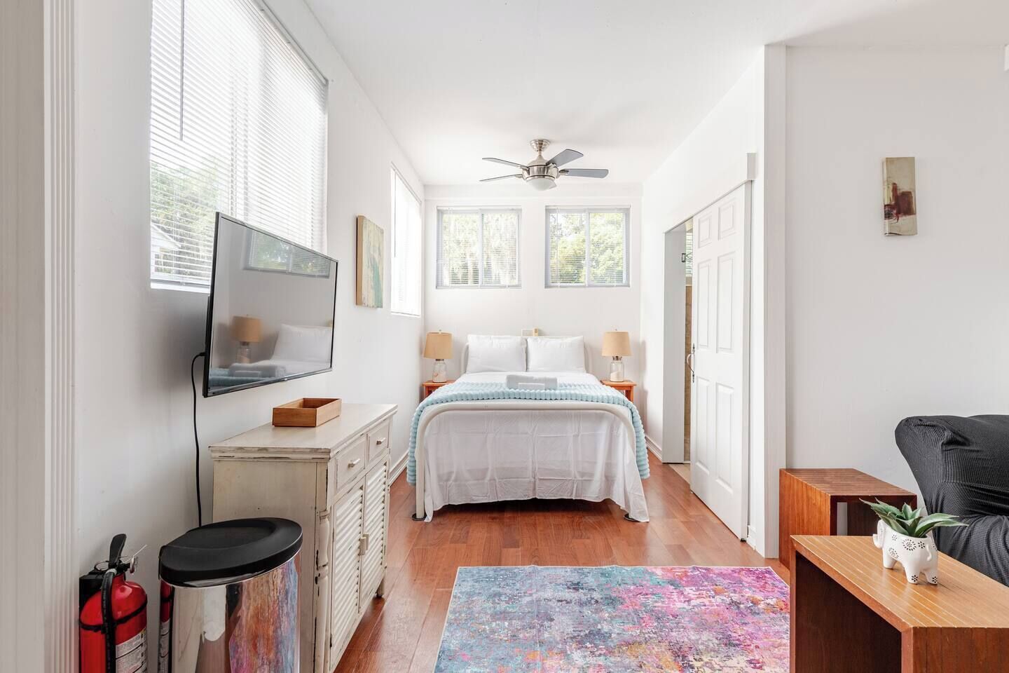 A bedroom with a bed, bedside tables, a ceiling fan, a window, and a door.