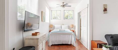 Un dormitorio con cama, mesitas de noche, ventilador de techo, ventana y puerta.
