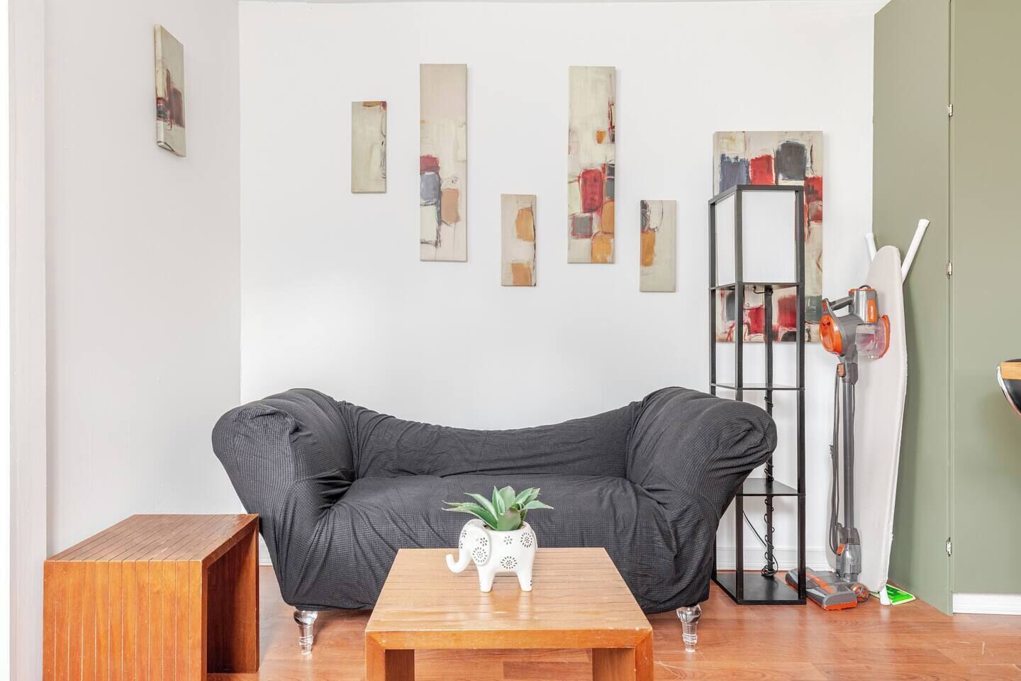 A living room with a black sofa, a wooden coffee table, and a white decorative pot.
