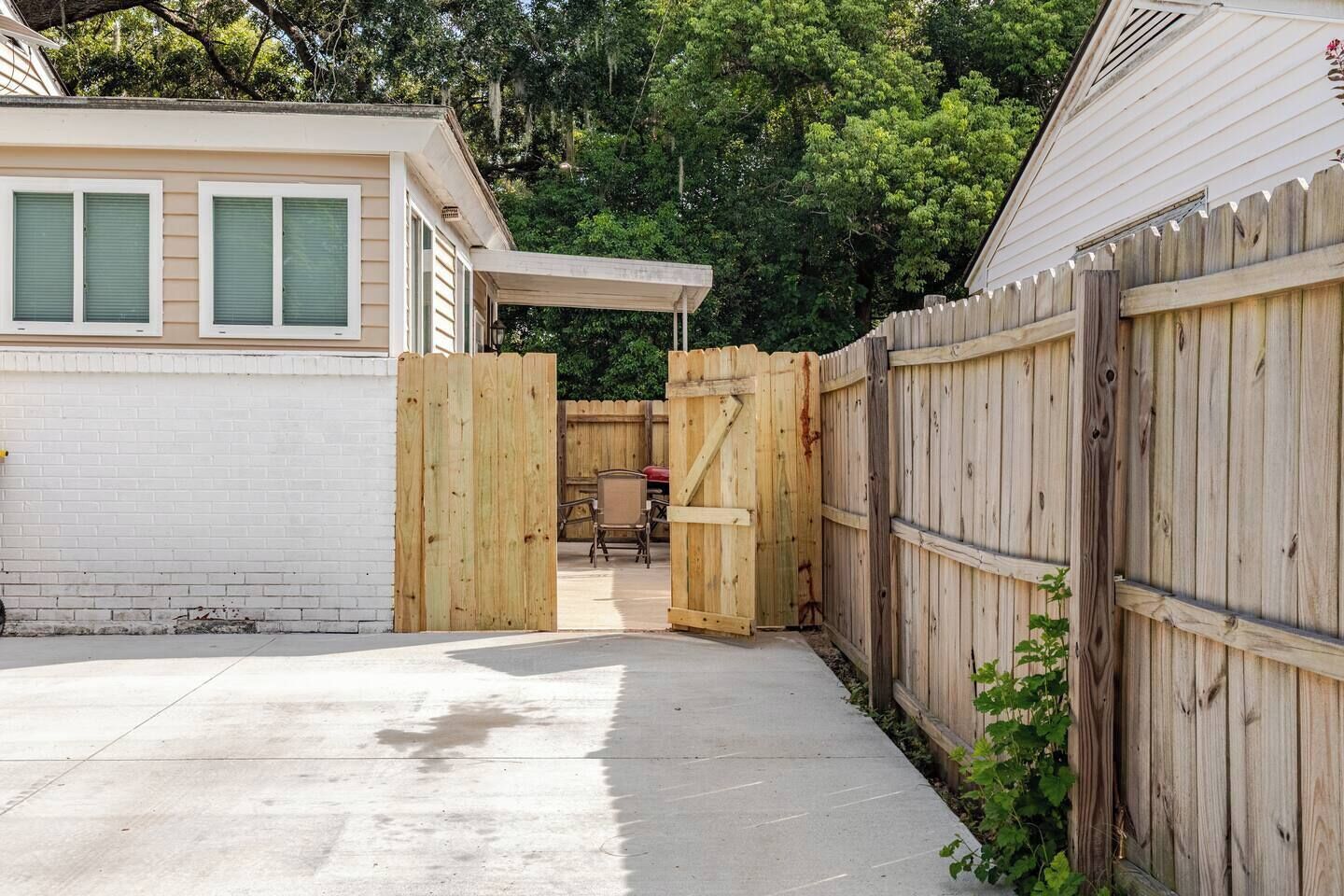 Un jardin avec une porte en bois, un espace patio et une maison à l’extérieur blanc.