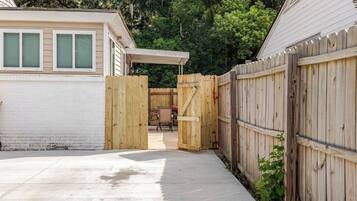 A backyard with a wooden gate, a patio area, and a house with a white exterior.