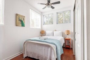 A bedroom with a bed, two bedside lamps, a ceiling fan, and a window with blinds.