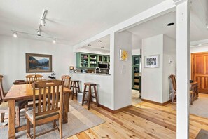A spacious dining area with a wooden table and chairs, a kitchen with green cabinets, and a painting on the wall. - Peaceful Elkhorn Aspen Retreat with Amenity Access (Sun Valley)