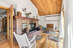 Een gezellige woonkamer met een schouw van baksteen, wit rieten meubilair en een houten plafond.