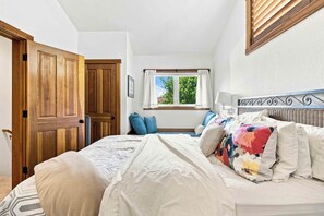 Une chambre à coucher avec un lit, une fenêtre avec des rideaux, une porte en bois et une tête de lit ornée d’un cadre en métal décoratif.