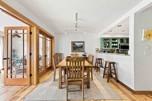 Un coin repas avec une table et des chaises en bois, un tableau au mur et une cuisine avec des meubles verts.