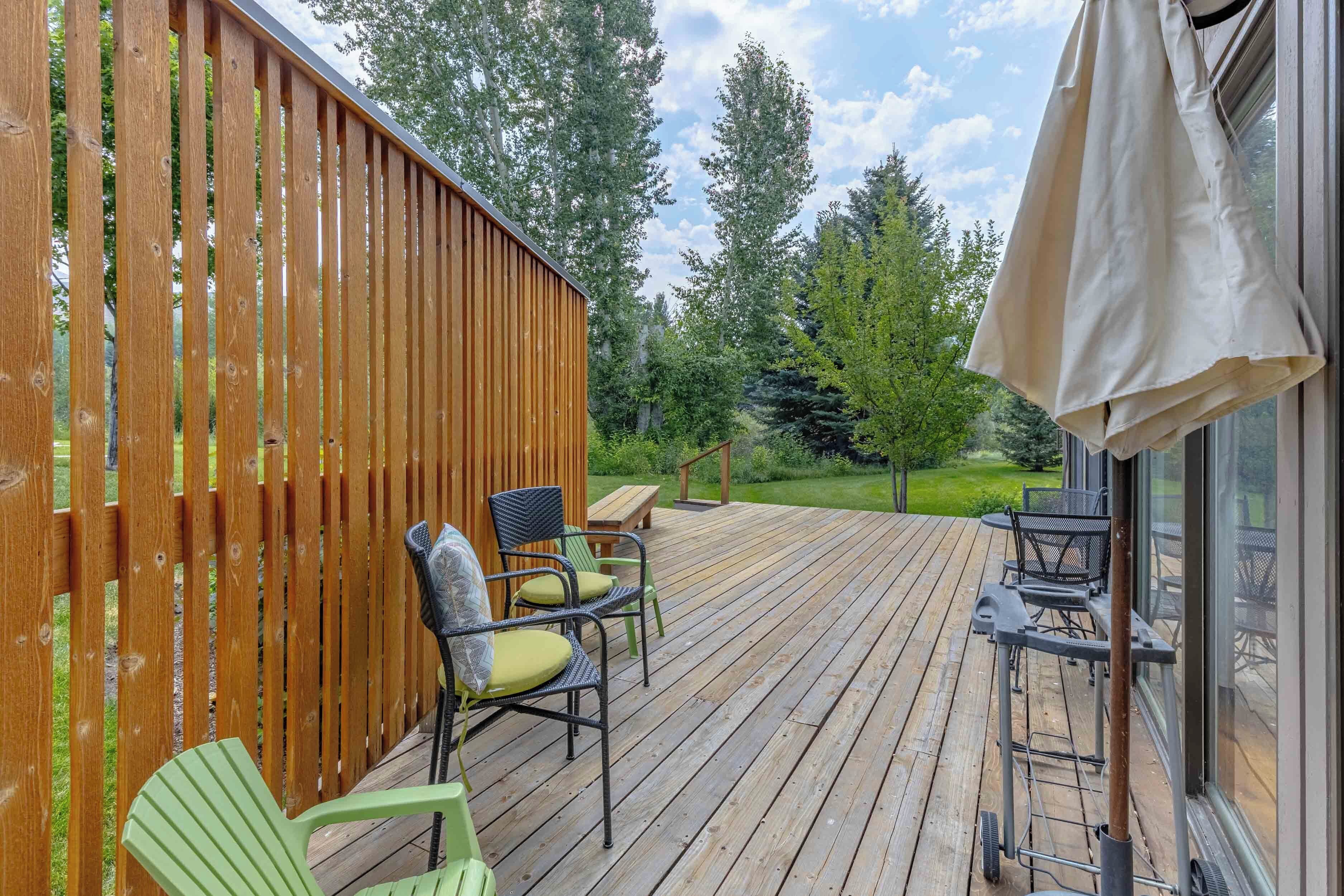 A wooden deck with outdoor furniture, a pergola, and a view of a forested area.
