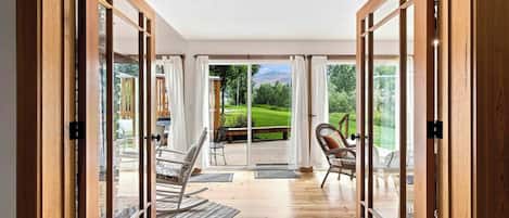 A room with a wooden floor, a sliding glass door leading to an outdoor deck with a view of a green landscape.
