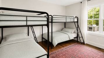 Une chambre avec des lits superposés, une fenêtre donnant sur un paysage verdoyant et un tapis à motifs.