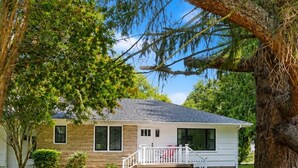 A single-story house with a front porch, a fenced yard, and a large tree in the foreground. - Home in Union Pier, MI (Union Pier)