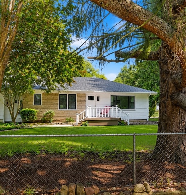 A single-story house with a front porch, a fenced yard, and a large tree in the foreground.