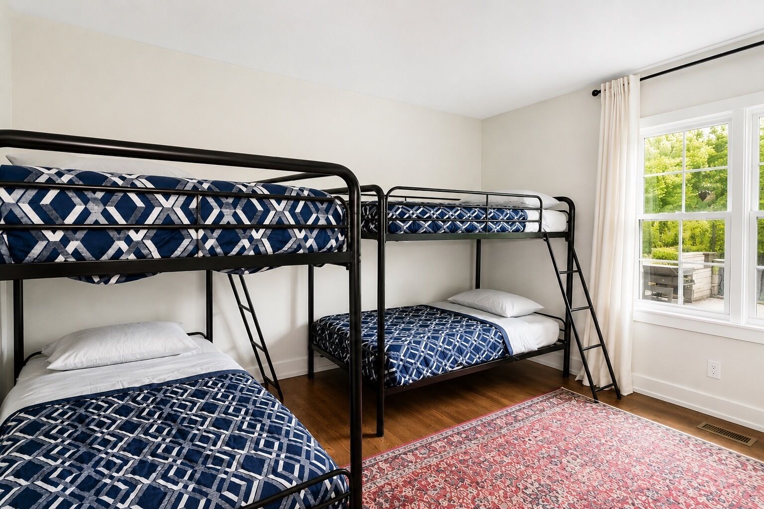 Une chambre avec des lits superposés, une fenêtre avec des rideaux et un tapis à motifs.