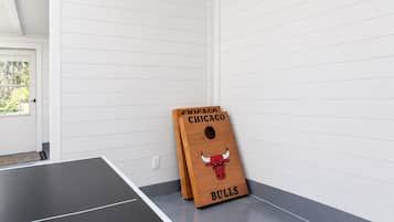 Une table de ping-pong dans une pièce aux murs recouverts de panneaux blancs, avec une porte donnant sur un paysage verdoyant.