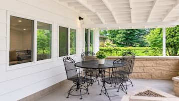 A covered patio with a round table and chairs, large windows, and a stone fire feature.