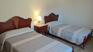 A hotel room with two single beds, a nightstand with a lamp, and a plain wall. - Casa Lago-Marí — Large house near the sea (Lariño)