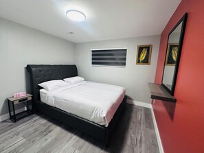 Une chambre à coucher avec un lit, une table de chevet, un miroir et une fenêtre avec des stores.