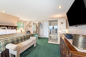A hotel room with a bed, bench, desk, and a television.