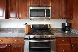 A kitchen with wooden cabinets, a stainless steel stove, a microwave, and a coffee maker. - New! Stunning Lake & Mountain Views, Sauna, Backyard, Walk to Downtown Polson! (Polson)