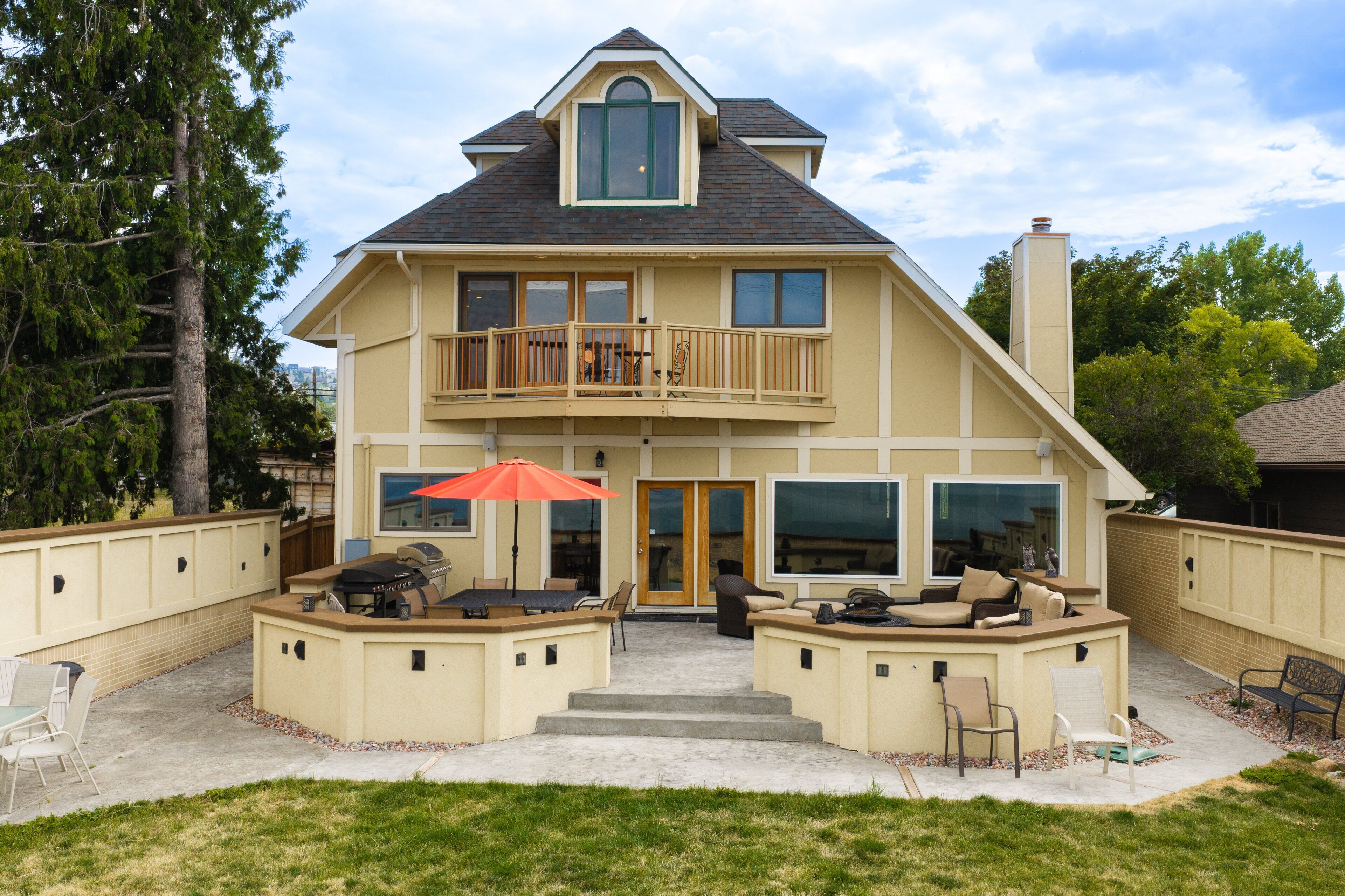 A two-story house with a balcony, a patio with outdoor furniture, and a large window.