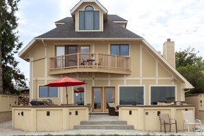 A two-story house with a balcony, a patio with outdoor furniture, and a chimney. - New! Stunning Lake & Mountain Views, Sauna, Backyard, Walk to Downtown Polson! (Polson)