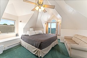 A bedroom with a bed, a ceiling fan, a window with curtains, a chair, and a view of the outdoors. - New! Stunning Lake & Mountain Views, Sauna, Backyard, Walk to Downtown Polson! (Polson)