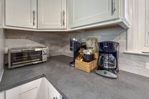 Una cocina con alacenas blancas, horno tostador, cafetera y una cesta con objetos.