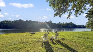 Un césped con un lago, sillas y una mesa bajo un árbol.