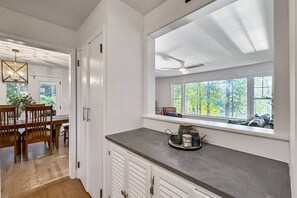 Une cuisine avec un coin fenêtre, un espace repas avec des chaises en bois et un ventilateur de plafond.
